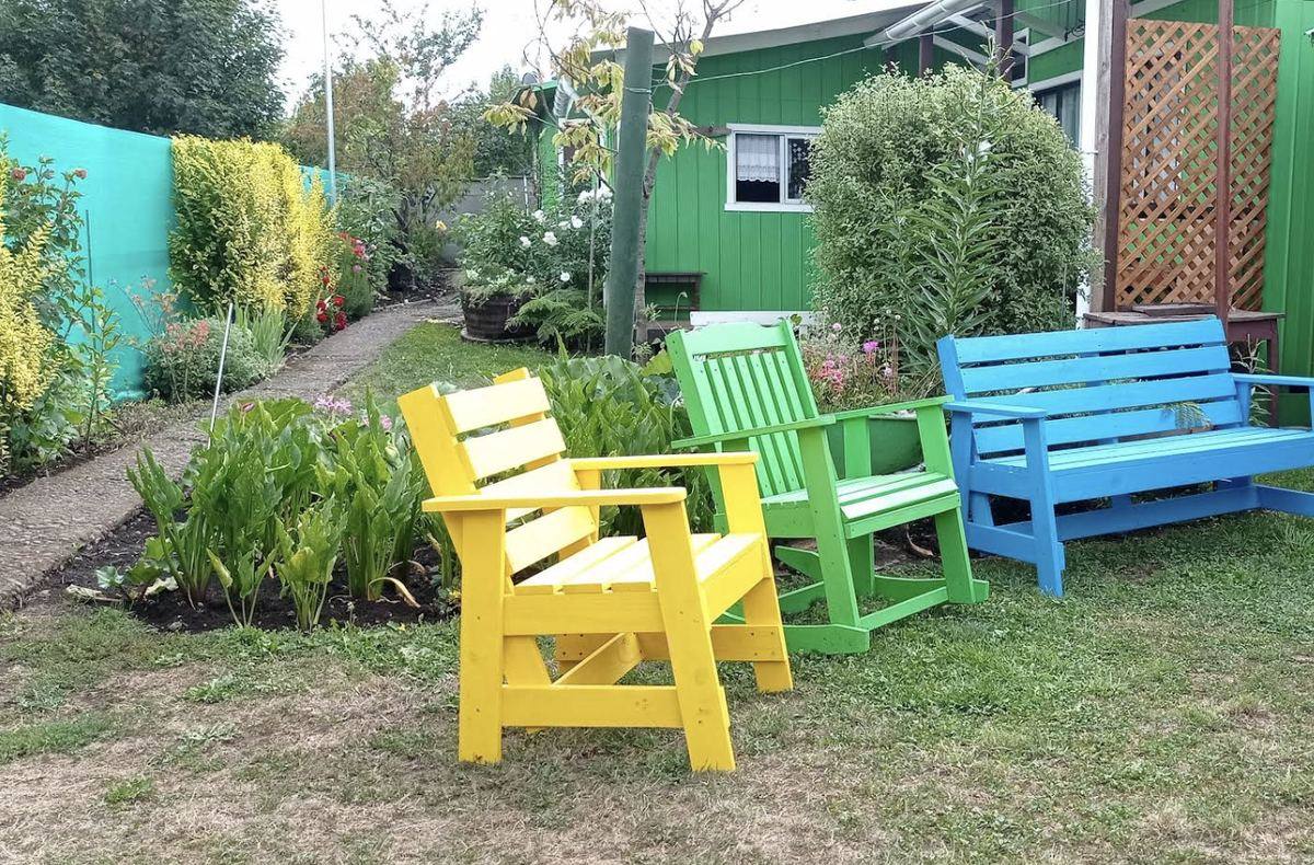 Escaños de madera pintados de amarillo, verde y azul en el jardín